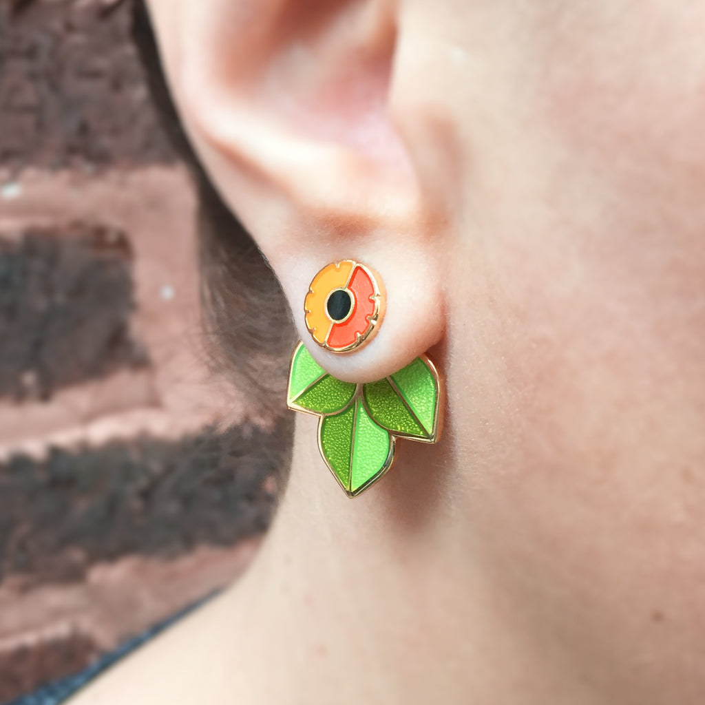 Close up of a person wearing Anenome enamel flower studs with leaf jacket earrings seconds.