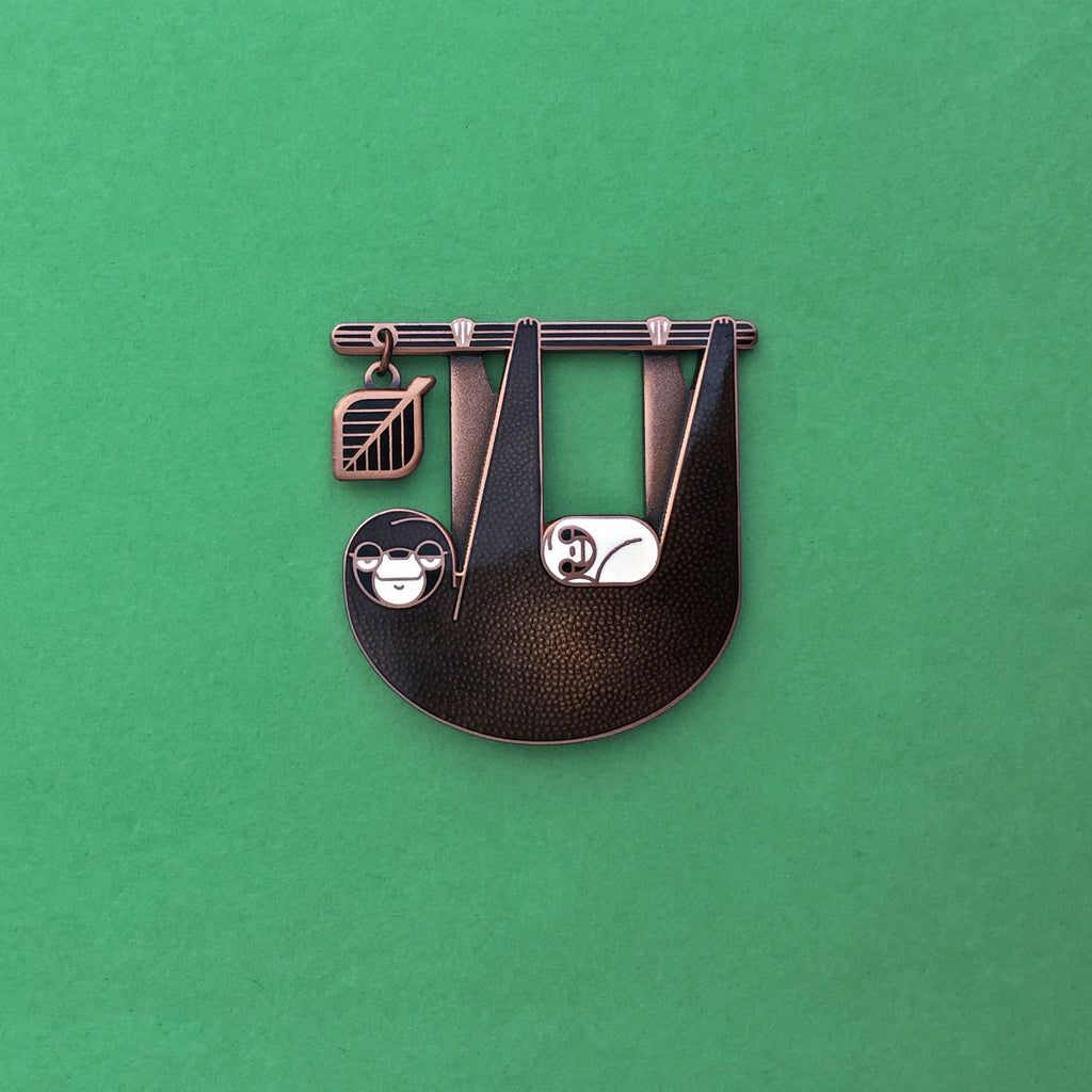 Slothlorien sloth and sleeping cub enamel pin seconds in antique copper. Black enamel, with white cub and leaf dangle.